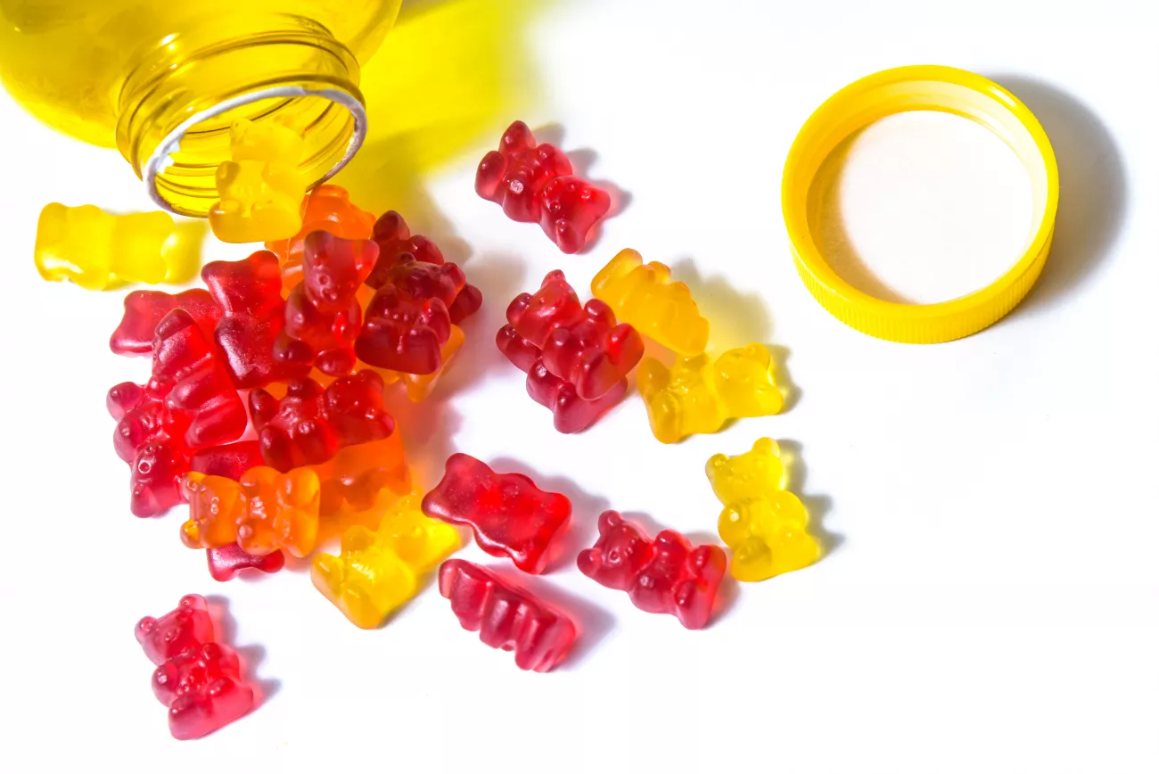 Gummy bears lay scattered around the mouth of an open bottle.