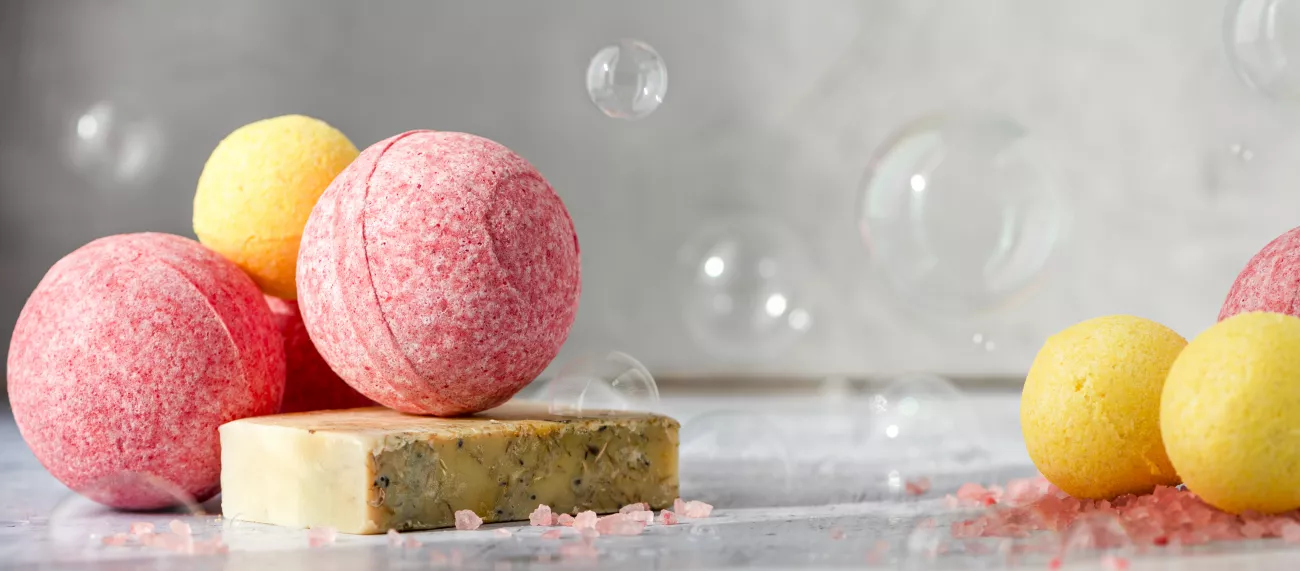 An array of bath bombs are displayed on a counter surrounded by floating bubbles.