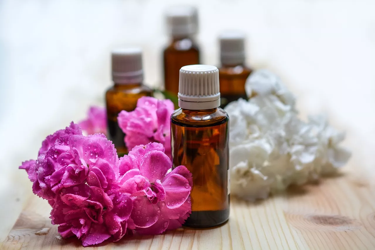 Bottles of oils are surrounded by pink and white flowers.
