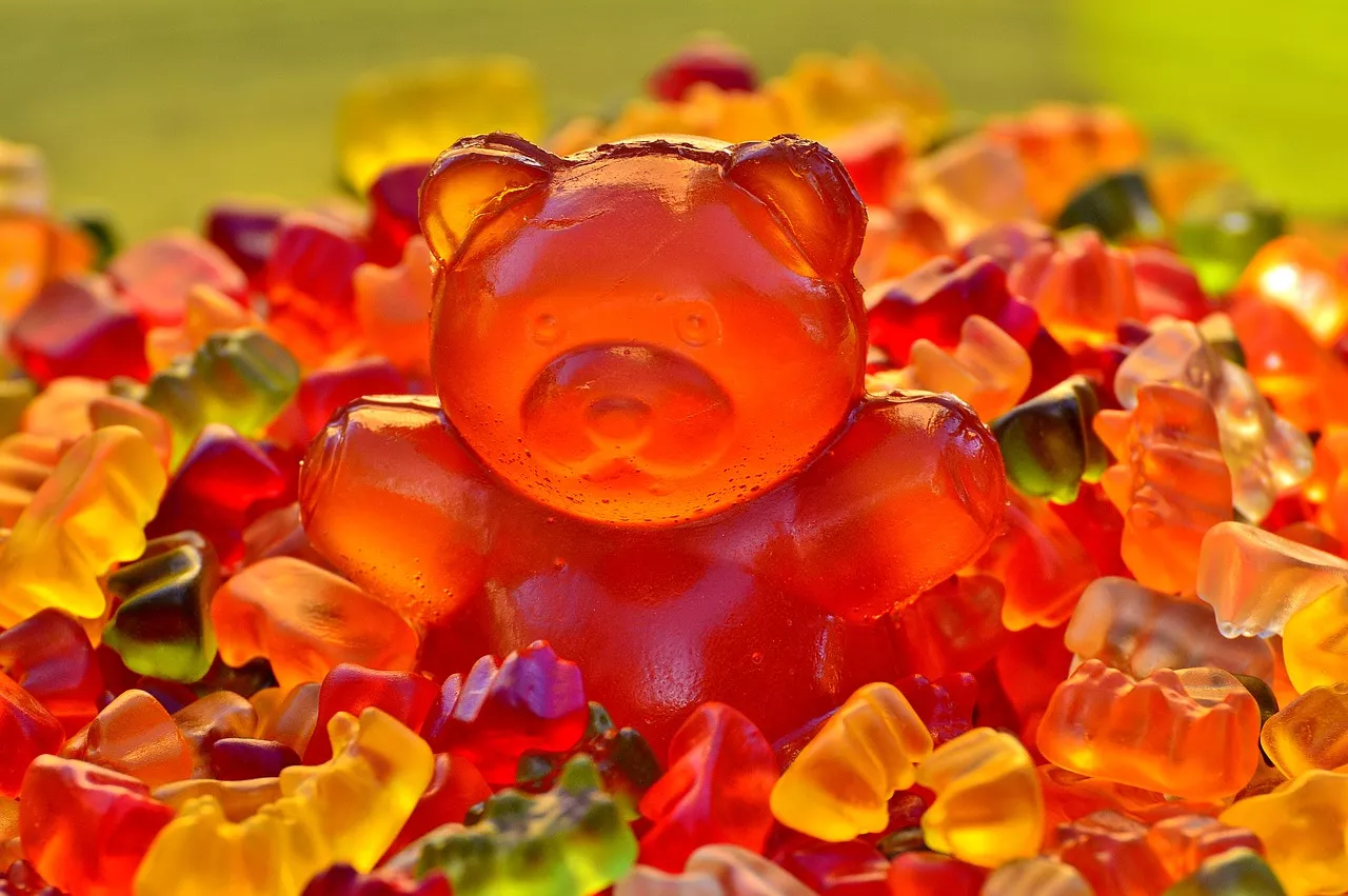 Small colorful gummy bears are piled around a giant gummy bear.