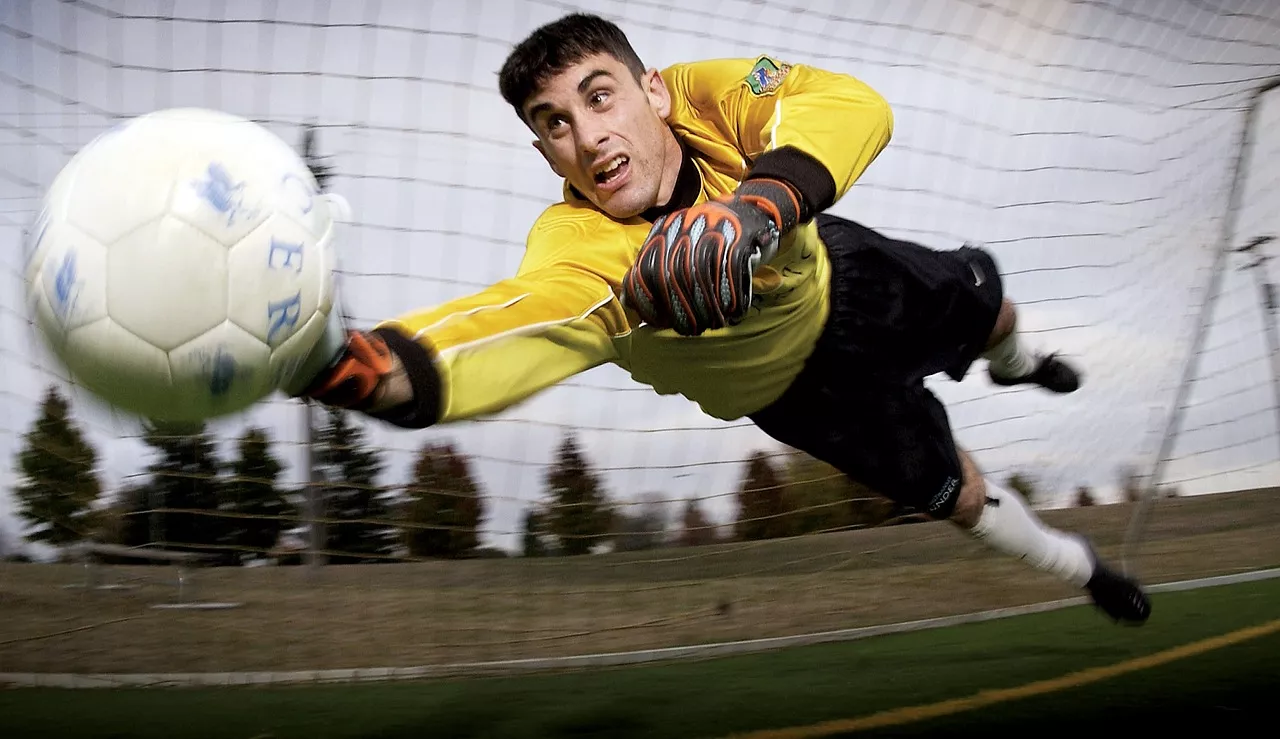 An athletic soccer goalie is blocking the ball.